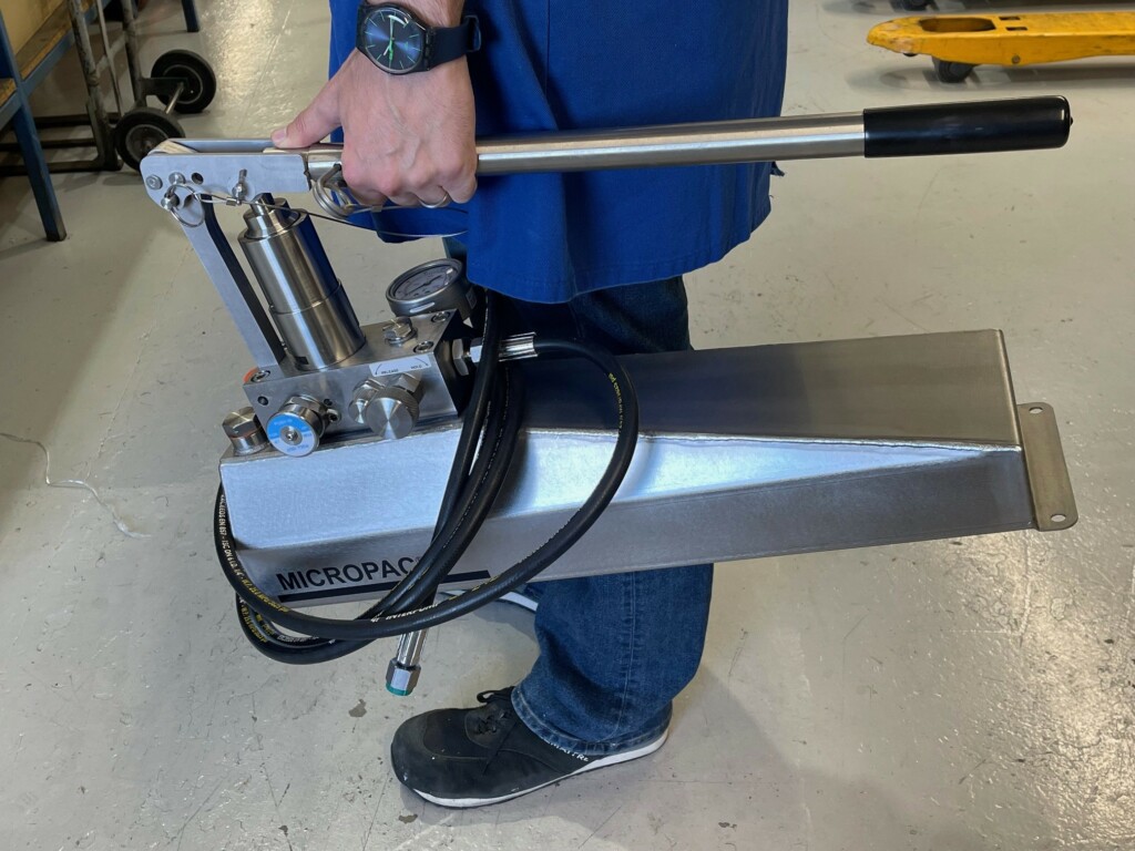 A person carrying a stainless steel Micropac pressure test pump to their job