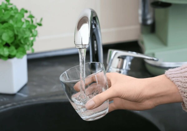 Hand holding a glass under a running tap filling it with clear and fresh drinking water.